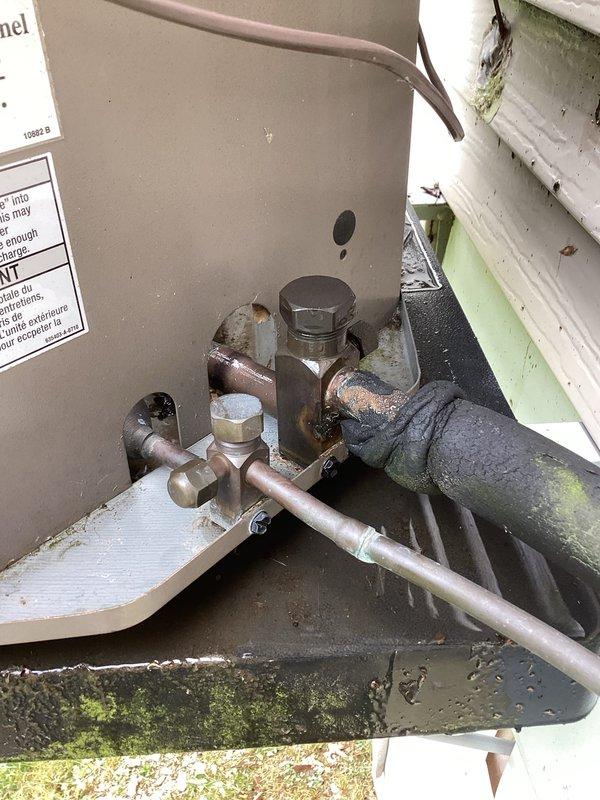 Responded to no cooling complaint on aging residential air conditioning system. Upon arrival, found ice buildup on exterior refrigerant lines and unit not producing cold air. Documented outdoor condensing unit condition showing weathered components, oxidized copper refrigerant lines, and aged equipment connections consistent with 10+ year old system. Unit was already turned off by customer prior to arrival due to freezing condition. Inspected exterior grille, refrigerant line connections, and overall equipment condition to assess system status and determine appropriate next steps for restoring cooling operation.