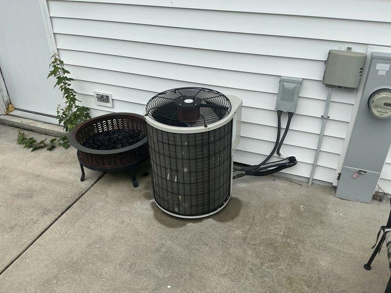 Completed comprehensive site assessment for full HVAC system replacement including furnace and air conditioning unit. Evaluated existing outdoor condenser unit with cylindrical design and top-discharge fan configuration, noting electrical disconnect and meter connections on exterior wall. Inspected indoor furnace installation area, documenting existing ductwork plenum with visible condensation indicating potential insulation deficiencies, and assessed structural framing and workspace access for equipment removal and installation. Photographed current system configuration and prepared detailed replacement estimate for complete heating and cooling system upgrade.