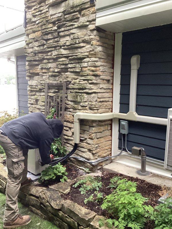 Completed installation of Mitsubishi mini-split heat pump system at residential property. Mounted outdoor condenser unit on concrete pad against stone exterior wall, installed refrigerant line set and electrical connections through exterior wall penetration, and routed condensate drainage via white PVC piping along building exterior. Indoor air handler installation included proper refrigerant charging, system commissioning, and operational testing to verify heating and cooling performance. All work performed in accordance with manufacturer specifications and local permit requirements, with licensed electrician completing final electrical connections.