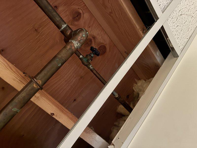 Completed diagnostic evaluation and replacement of two interior shut-off valves serving exterior hose bibs. Accessed valves located in concealed space behind ceiling/wall area with exposed framing. Removed existing corroded shut-off valves showing significant oxidation and patina buildup on copper supply lines. Installed new shut-off valves with cross-handle mechanisms on copper piping connections to ensure proper water control to outdoor spigots. Verified proper operation of both new shut-off valves and confirmed no leaks at connection points.