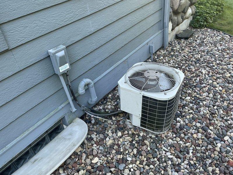Conducted comprehensive assessment of existing HVAC system for replacement estimate, including outdoor air conditioning condenser unit with cylindrical configuration and indoor gray metal furnace with associated PVC venting. Evaluated current equipment operation, photographed installation details of both exterior AC unit on decorative stone base with electrical disconnect and refrigerant lines, and interior furnace positioned alongside water heater in basement utility area. All equipment confirmed operational at time of inspection, providing customer with replacement options and system upgrade recommendations.