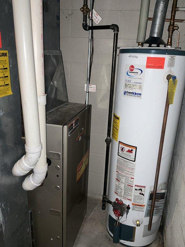 Conducted comprehensive assessment of existing HVAC system for replacement estimate, including outdoor air conditioning condenser unit with cylindrical configuration and indoor gray metal furnace with associated PVC venting. Evaluated current equipment operation, photographed installation details of both exterior AC unit on decorative stone base with electrical disconnect and refrigerant lines, and interior furnace positioned alongside water heater in basement utility area. All equipment confirmed operational at time of inspection, providing customer with replacement options and system upgrade recommendations.