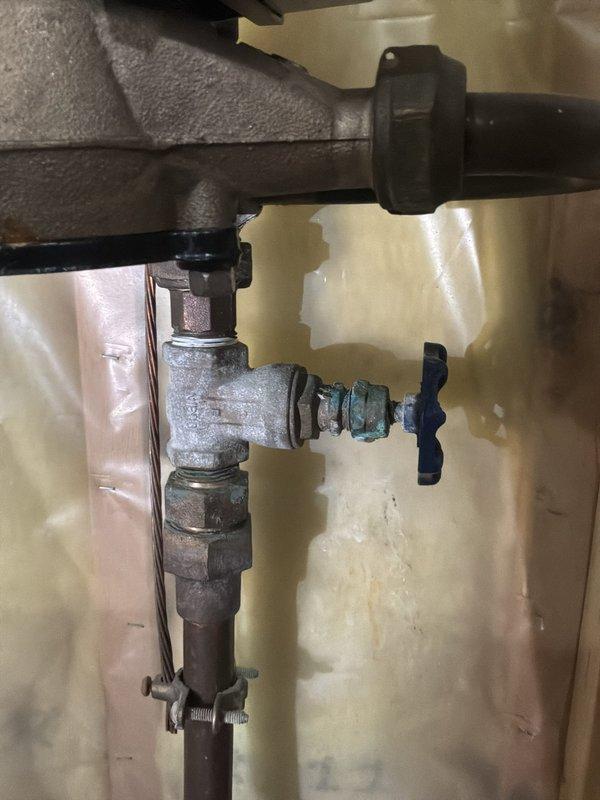 Conducted on-site assessment for replacement of two aging shutoff valves located on both sides of the water meter in basement. Inspection revealed existing valves showing signs of corrosion, oxidation, and weathering, with visible verdigris on copper components and deteriorated metal surfaces. Documented current plumbing configuration including vertical pipe assembly with compression fittings, valve bodies with blue handles, and associated copper tubing secured with mounting brackets. Noted water staining on adjacent wall surfaces indicating potential past leakage or moisture exposure. Photographed existing valve conditions, pipe connections, threaded fittings, and overall meter assembly to provide accurate estimate for valve replacement work. Observed water treatment system including softener unit with salt supply in immediate vicinity of work area. Provided detailed assessment of required materials and labor for complete shutoff valve replacement to ensure proper water meter isolatio