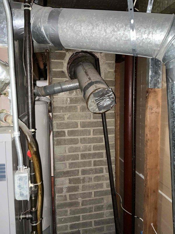 Conducted on-site assessment for water heater replacement in mechanical room with exposed brick construction. Documented existing installation including copper and PVC plumbing connections, exhaust venting through masonry wall, and clearance measurements of approximately 6.5 inches between HVAC ductwork and equipment mounting location. Photographed current configuration to prepare replacement estimate.