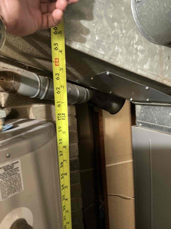 Conducted on-site assessment for water heater replacement in mechanical room with exposed brick construction. Documented existing installation including copper and PVC plumbing connections, exhaust venting through masonry wall, and clearance measurements of approximately 6.5 inches between HVAC ductwork and equipment mounting location. Photographed current configuration to prepare replacement estimate.