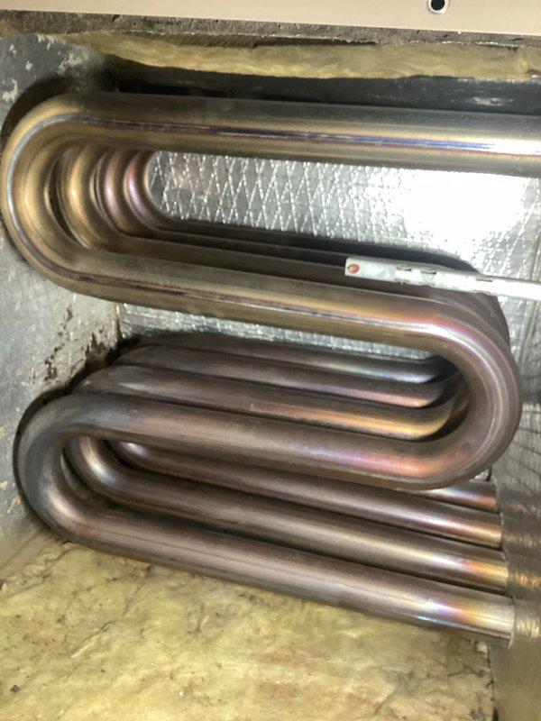 Responded to service call for Magicpak-179 unit with water leakage affecting the unit below. Performed inspection of both sides of the vertical stack HVAC system installed in confined utility space. Examined serpentine heat exchanger coils showing heat discoloration and inspected condensate drainage system including white PVC piping. Identified source of water intrusion and cleared condensate drain line blockage to resolve leakage issue. Verified proper drainage flow, checked air handler components, and confirmed system operation. Unit restored to normal function with no further water discharge into lower unit.
