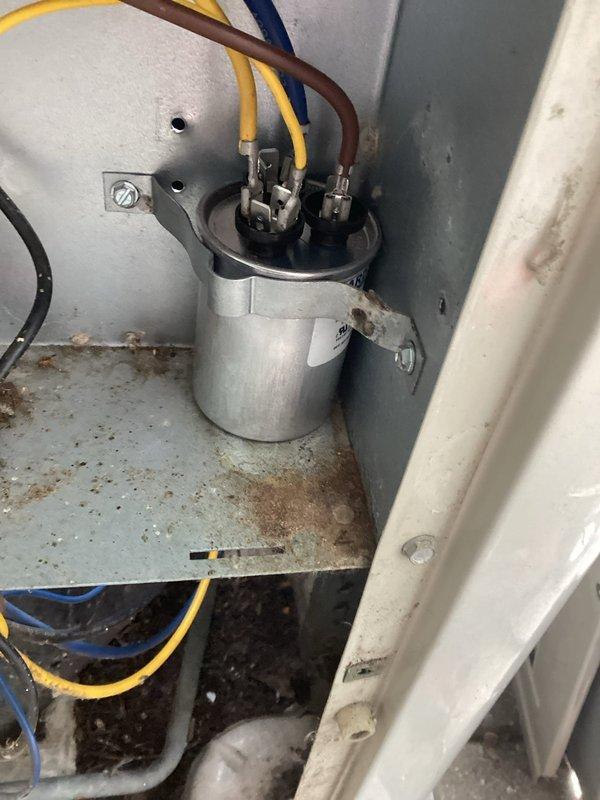 Responded to no cooling call on aging air conditioning system. Upon inspection, found failed dual run capacitor with visible corrosion and rust staining on mounting surface, preventing compressor and condenser fan motor operation. Replaced defective capacitor, verified proper electrical connections, and tested system operation with successful cooling restored.