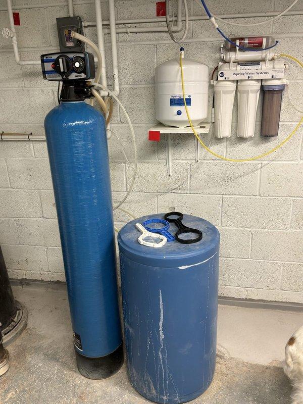 Conducted on-site evaluation for water softener installation in residential property with existing water treatment infrastructure. Assessed current plumbing configuration in crawl space and basement utility area, including copper supply lines, drainage systems, and existing Sterling Water Systems reverse osmosis filtration unit with wall-mounted pressure tank. Documented existing two-tank water treatment system setup and available connection points for proposed water softener integration with current HVAC equipment and water heater installations.