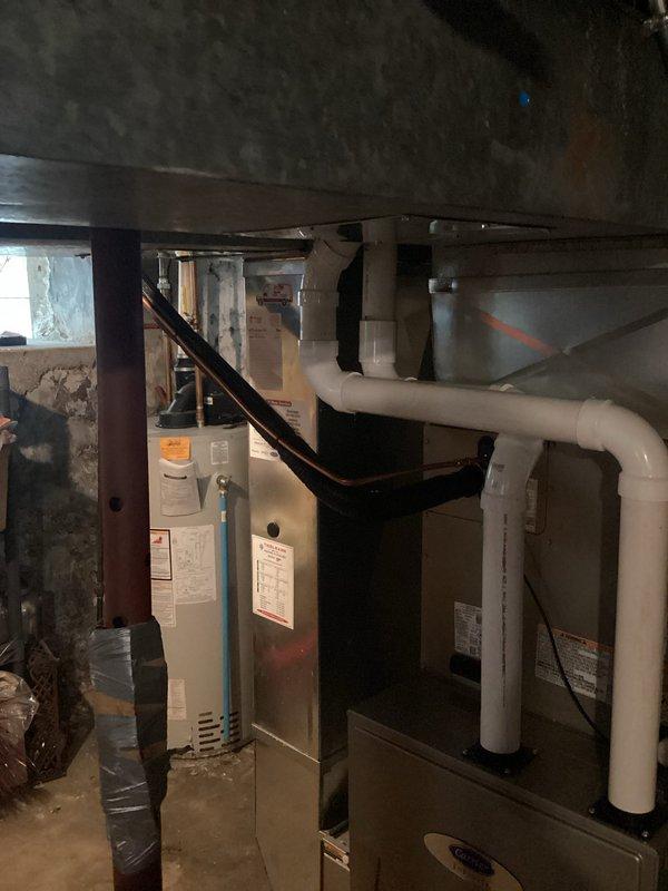 Completed installation of new Carrier air conditioning condenser unit with matching evaporator coil and 15-foot refrigerant line set. The outdoor condenser was mounted on a composite pad against the building exterior with proper clearances, and copper refrigerant lines were routed along the siding to connect with the indoor evaporator coil installed above the existing furnace in the basement. All electrical connections, refrigerant lines, and condensate drainage were completed per manufacturer specifications, and the system was charged, tested, and verified operational.
