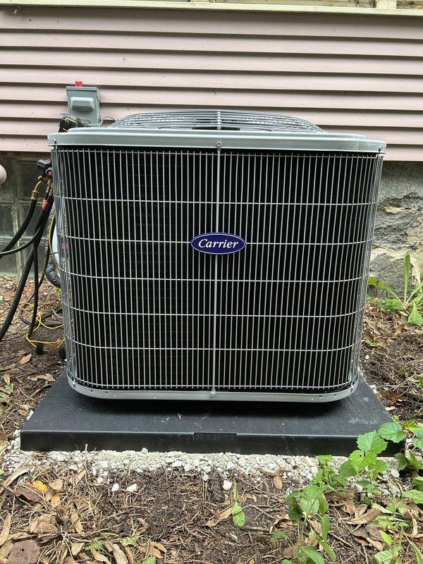Completed installation of new Carrier air conditioning condenser unit with matching evaporator coil and 15-foot refrigerant line set. The outdoor condenser was mounted on a composite pad against the building exterior with proper clearances, and copper refrigerant lines were routed along the siding to connect with the indoor evaporator coil installed above the existing furnace in the basement. All electrical connections, refrigerant lines, and condensate drainage were completed per manufacturer specifications, and the system was charged, tested, and verified operational.