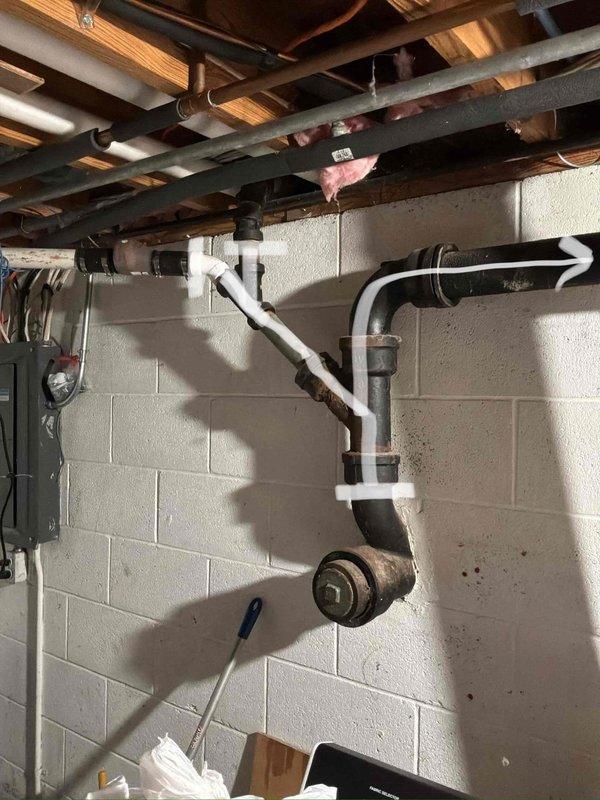 Conducted comprehensive assessment of existing sewer stack system in basement area. Inspected severely corroded cast iron drain pipes showing extensive rust deterioration throughout multiple joints, elbows, and connection points. The existing piping configuration exhibited significant age-related degradation with reddish-brown corrosion compromising structural integrity of the drainage system. 

Documented current plumbing infrastructure including horizontal and vertical pipe runs mounted between floor joists, noting multiple right-angle connections and elbow fittings in deteriorated condition. Evaluated replacement scope requiring removal of compromised cast iron stack and installation of new PVC drainage piping system to restore proper waste water flow and prevent potential leaks or failures.