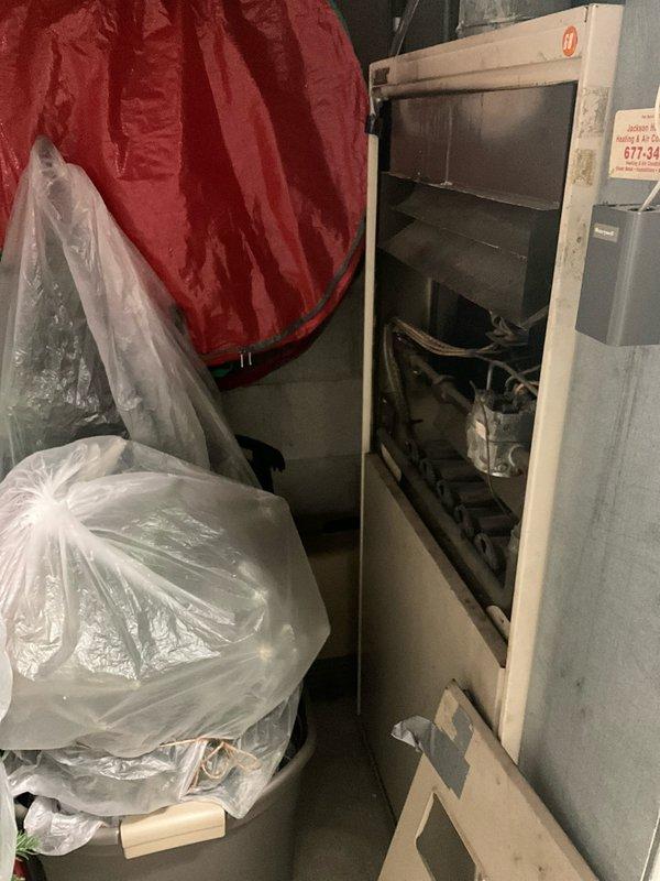 Conducted on-site evaluation of 50-year-old Lennox natural gas furnace located on first floor of raised ranch home. Unit currently operational but has reached end of expected service life. Assessed existing installation in rear utility area, documented equipment configuration and clearances. Photographed current furnace setup showing cabinet-style installation with mechanical components, venting, and gas connections. Provided comprehensive replacement estimate for new high-efficiency natural gas furnace system including removal of existing unit, installation of modern equipment, and necessary modifications to meet current code requirements.