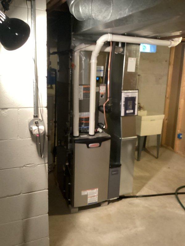 Completed full HVAC system installation including new furnace, air conditioning unit, and water heater in residential basement location. All required permits were obtained prior to work commencement, and licensed electrician provided necessary electrical connections to ensure code compliance. New gray furnace unit was installed with proper PVC venting routed vertically through structure, copper refrigerant lines configured with appropriate service loops, and metal supply/return ductwork connected to existing distribution system. Air handler and condensing unit were positioned for optimal airflow and serviceability. Water heater installation completed with required safety devices and proper venting. All equipment tested for proper operation, refrigerant charge verified, combustion analysis performed on gas-fired appliances, and system commissioned successfully. Work area left clean and organized with all components functioning within manufacturer specifications.