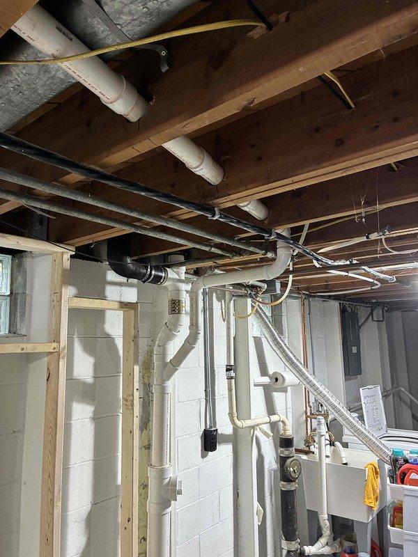 Completed rough-in plumbing installation for new full bathroom addition in unfinished basement. Installed complete drainage system including PVC waste lines routed through ceiling joists and vertical drain stacks mounted to concrete block walls. Ran water supply lines utilizing both PVC and copper piping to accommodate future fixture locations. Poured and leveled concrete floor sections in cross-pattern configuration to establish proper drainage slopes and prepare substrate for fixture installation. Coordinated plumbing rough-in with existing HVAC ductwork and electrical systems in ceiling space to ensure proper clearances and code compliance.