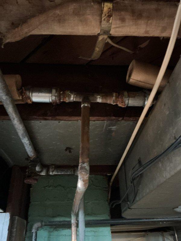 Completed assessment and sold repiping repair for residential plumbing system showing significant deterioration. Inspected corroded galvanized piping with extensive rust buildup on horizontal runs and vertical drops, along with aging P-trap assembly beneath fixture. Documented deteriorated metal pipe infrastructure in utility area with compromised fittings and joints exhibiting orange-brown corrosion throughout. Recommended complete repiping solution to address failing galvanized lines and prevent future leaks or water quality issues.