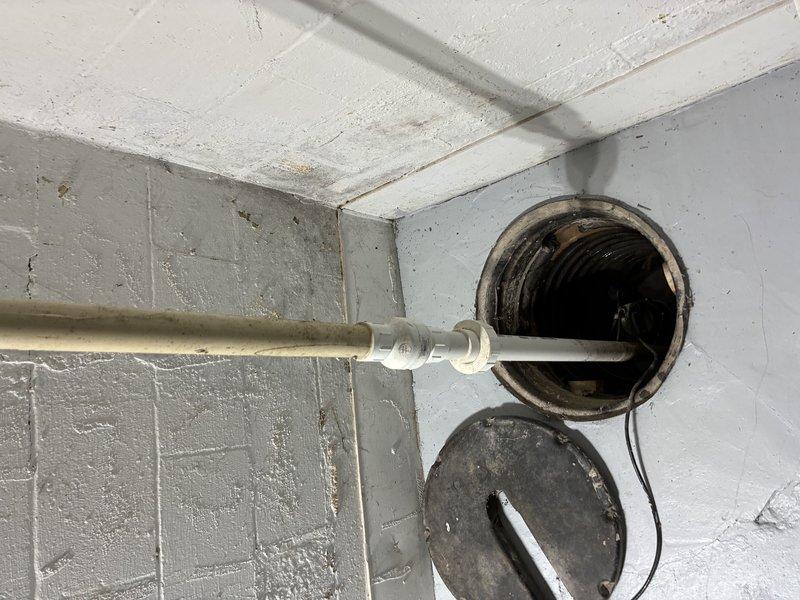 Responded to service call for sump pump issues at residential property. Upon arrival, conducted thorough inspection of basement utility area and sump pump system. Examined discharge piping system, including horizontal PVC drainage lines and mounting hardware secured to concrete block walls. Inspected ceiling-mounted piping infrastructure and verified proper slope and support of discharge lines. Evaluated ventilation opening and associated ductwork in utility space for proper clearance and functionality. Assessed overall condition of plumbing connections, joints, and elbow fittings throughout the sump pump discharge system. Documented existing conditions with photographs for service records. System components showed normal wear consistent with age of installation. All piping connections and mounting brackets were secure and functioning as designed.