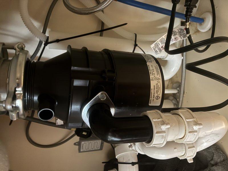 Installed new garbage disposal unit beneath kitchen sink per customer estimate. Connected disposal to existing sink drain flange and integrated unit with white PVC drain line configuration including P-trap assembly. Completed electrical connection via junction box with flexible metal conduit, secured all plumbing connections with appropriate fittings and clamps, and verified proper operation of the disposal system.