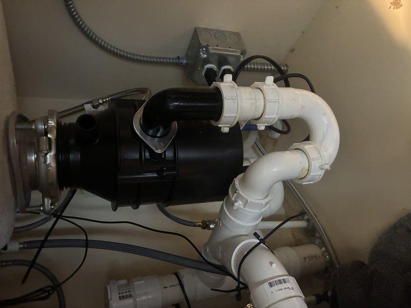 Installed new garbage disposal unit beneath kitchen sink per customer estimate. Connected disposal to existing sink drain flange and integrated unit with white PVC drain line configuration including P-trap assembly. Completed electrical connection via junction box with flexible metal conduit, secured all plumbing connections with appropriate fittings and clamps, and verified proper operation of the disposal system.
