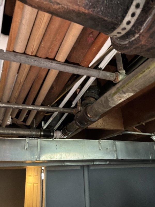 Conducted comprehensive whole-house repipe estimate for residential property requiring replacement of existing iron supply piping with copper and outdated drain lines with PVC. Assessed basement utility area with exposed ceiling joists, documenting current plumbing infrastructure including existing metal pipes, HVAC ductwork, and structural layout to determine scope of work for complete piping system replacement.
