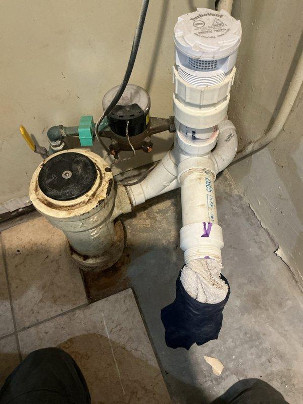 Responded to service call for reported water leak in basement utility area. Upon arrival, performed diagnostic inspection of plumbing assembly consisting of white PVC piping with multiple fittings and connections arranged vertically along corner wall. Identified older-style valve component at base of assembly showing significant age-related deterioration, including visible corrosion, rust-colored staining, and discoloration around circular face and body. Examined PVC pipe connections, threaded fittings, and flow meter device with monitoring equipment. Inspected junction points where vertical pipe connects to elbow joint and horizontal runs, noting wear patterns and residue accumulation around connection points. Documented condition of plumbing system through photographic evidence for estimate preparation. Leak source assessment completed, findings indicate compromised valve assembly requiring replacement to resolve water intrusion issue.