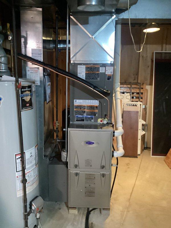 Completed full installation of new air conditioning system and evaporator coil with 24-foot refrigerant line set connecting outdoor condensing unit to indoor air handler. Modified and raised existing ductwork in basement mechanical room to accommodate new equipment configuration. Coordinated with licensed electrician for proper electrical connections and obtained necessary permits for installation compliance. Installed Carrier-branded indoor unit in basement alongside existing water heater, ensuring proper clearances and accessibility for future maintenance. Positioned outdoor condensing unit on exterior pad adjacent to house foundation with appropriate clearance from structure and landscaping. Verified all refrigerant connections, tested system operation, and confirmed proper airflow through modified duct system. System commissioned and operating to manufacturer specifications.