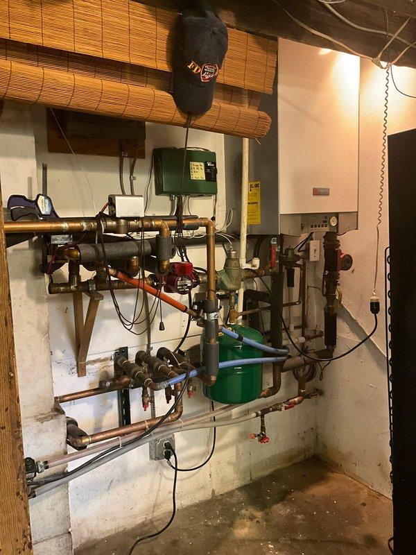 Conducted estimate for boiler replacement on existing 20-year-old high-efficiency unit that is currently operational. System includes extensive copper manifold piping with multiple zone valves and does not have an indirect water heater tank. Assessed existing white wall-mounted boiler with digital display panel, associated circulator pumps, and zone control components mounted in basement mechanical room. Evaluated current piping configuration, electrical connections, venting system, and overall installation layout to provide replacement recommendations and specifications for new high-efficiency boiler system.