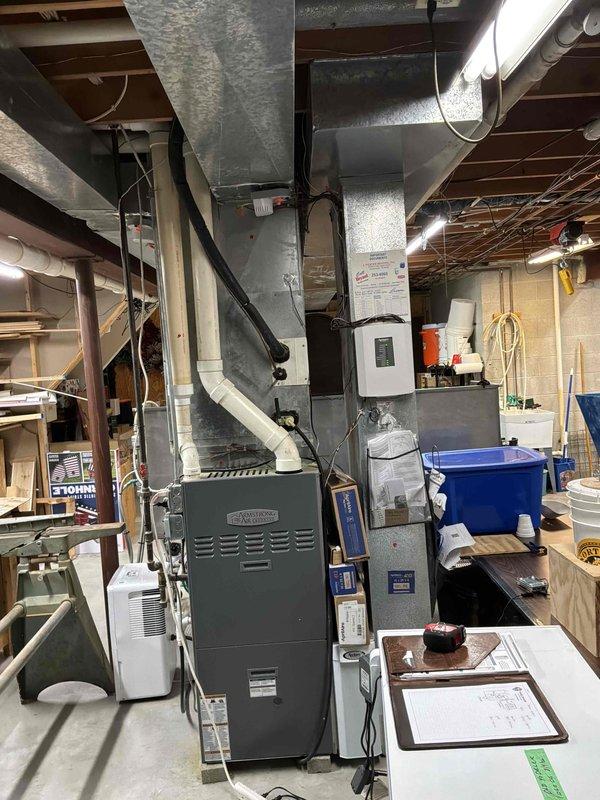 Conducted on-site evaluation for complete HVAC system replacement including existing furnace, air conditioning unit, and potential water heater upgrade. Assessed current equipment configuration with furnace located in basement mechanical room, documented existing ductwork layout and spatial constraints, and evaluated feasibility of relocating furnace to optimize system performance and accessibility. Photographed existing gray furnace unit with connected ductwork system and outdoor white condenser unit with protective grille to document current installation conditions for replacement proposal development.