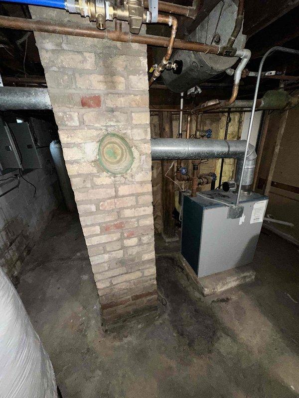 Conducted on-site assessment for boiler replacement in residential basement mechanical room. Evaluated existing heating system including current boiler unit, chimney flue configuration, electrical panel capacity, and distribution infrastructure. Documented equipment layout showing brick chimney stack, existing white boiler unit on concrete base, associated ductwork, copper piping connections, and electrical service panels. Assessed feasibility of adding zone control system for upper floor heating distribution. Photographed mechanical room conditions including electrical panels, HVAC components, and existing piping configurations to develop comprehensive replacement estimate and zoning upgrade options.