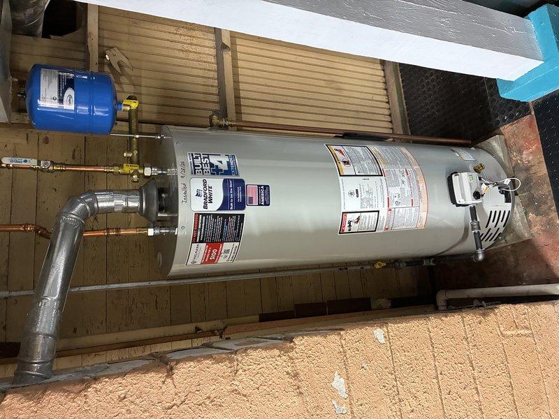 Installed a 40-gallon standard vent water heater with complete plumbing connections, including copper piping with shut-off valves and a wall-mounted blue expansion tank. The installation was completed in accordance with manufacturer specifications, with all safety components properly connected and the unit positioned on a tiled utility room floor with proper clearances maintained.