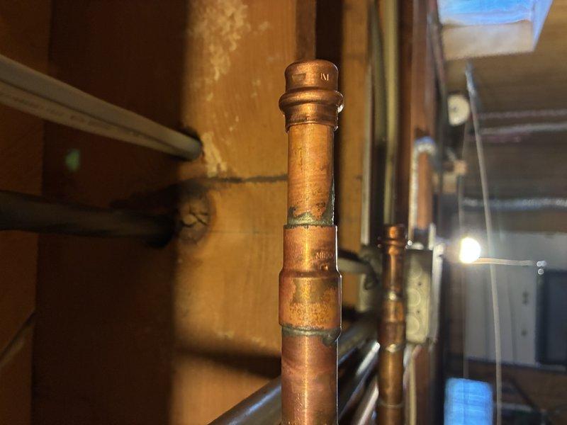 Responded to callback for reported dripping copper pipe. Upon arrival, inspected vertical copper plumbing system and associated connections in basement area. Located moisture on pipe surface and identified active drip at coupling joint near vertical run. Documented existing conditions with photos showing aged copper piping with visible patina, multiple connection points, and surrounding infrastructure including horizontal pipe runs and floor joists. Assessed joint integrity and connection points throughout accessible plumbing network to determine source and extent of leak.