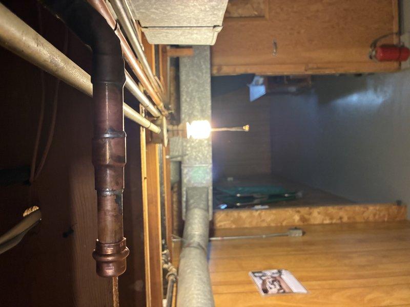Responded to callback for reported dripping copper pipe. Upon arrival, inspected vertical copper plumbing system and associated connections in basement area. Located moisture on pipe surface and identified active drip at coupling joint near vertical run. Documented existing conditions with photos showing aged copper piping with visible patina, multiple connection points, and surrounding infrastructure including horizontal pipe runs and floor joists. Assessed joint integrity and connection points throughout accessible plumbing network to determine source and extent of leak.