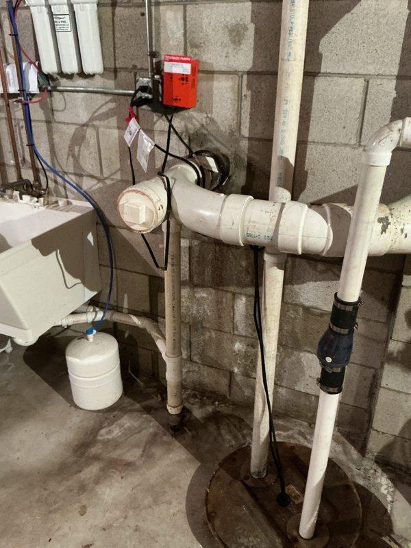 Responded to service call for water leakage along wall foundation originating from septic system piping. Upon arrival, conducted thorough diagnostic inspection of basement utility area and identified moisture intrusion patterns on concrete block walls. Documented existing plumbing infrastructure including sump pit assembly, PVC drainage lines, pressure tank, and pump control system. Traced water staining and discoloration on foundation walls to determine leak source and assess extent of water damage. Photographed affected areas showing septic piping connections, wall penetrations, and evidence of ongoing moisture issues for further evaluation and repair recommendations.