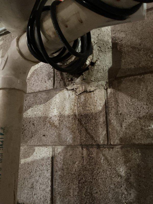 Responded to service call for water leakage along wall foundation originating from septic system piping. Upon arrival, conducted thorough diagnostic inspection of basement utility area and identified moisture intrusion patterns on concrete block walls. Documented existing plumbing infrastructure including sump pit assembly, PVC drainage lines, pressure tank, and pump control system. Traced water staining and discoloration on foundation walls to determine leak source and assess extent of water damage. Photographed affected areas showing septic piping connections, wall penetrations, and evidence of ongoing moisture issues for further evaluation and repair recommendations.