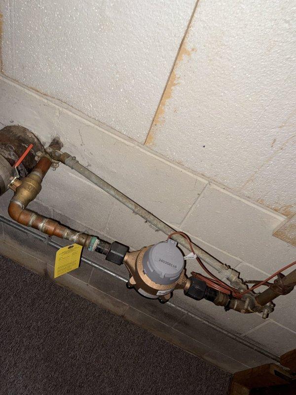 Completed comprehensive plumbing inspection of residential property, focusing on reported tub handle malfunction and evaluation for utility sink installation. Inspected main water supply system including water meter, shut-off valves, and copper distribution lines; noted age-related discoloration on piping and evidence of previous water intrusion on ceiling tiles near plumbing assembly. Examined tub fixture and identified loose handle requiring repair or replacement. Evaluated water heater and HVAC systems in basement utility area, confirming Bradford White water heater operational status with proper connections and safety components in place. Documented all findings with photographs and prepared estimate for requested utility sink addition.