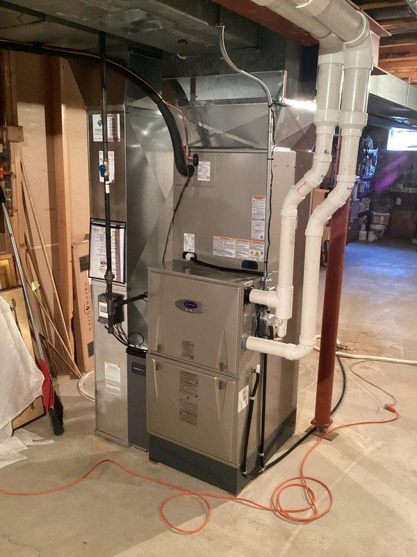 Completed full HVAC system installation in basement mechanical room, including new air conditioning unit, evaporator coil, and 43-foot refrigerant line set. Installed new Carrier-branded air handler unit mounted vertically above existing furnace, with proper integration of ductwork including white rigid supply ducts and black flexible return connections. Ran white PVC condensate drainage and venting pipes from system with appropriate routing through ceiling joists. Installed copper refrigerant lines along wall studs with proper insulation and secured mounting. Connected all electrical components to existing panel with code-compliant wiring. Coordinated with licensed electrician for electrical hookup and obtained necessary permits prior to installation. Tested system operation, verified proper airflow through metallic ductwork and galvanized plenum, confirmed refrigerant charge levels, and ensured all connections were secure and leak-free. System fully operational and ready for service.