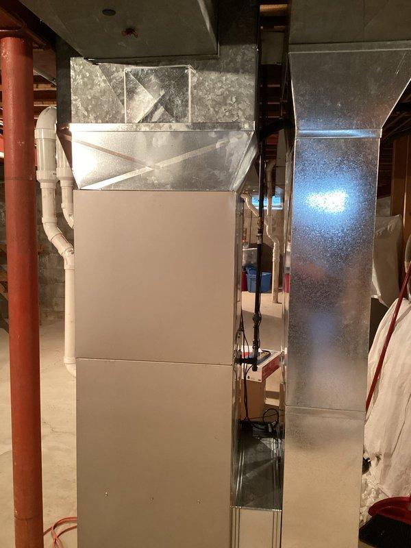 Completed full HVAC system installation in basement mechanical room, including new air conditioning unit, evaporator coil, and 43-foot refrigerant line set. Installed new Carrier-branded air handler unit mounted vertically above existing furnace, with proper integration of ductwork including white rigid supply ducts and black flexible return connections. Ran white PVC condensate drainage and venting pipes from system with appropriate routing through ceiling joists. Installed copper refrigerant lines along wall studs with proper insulation and secured mounting. Connected all electrical components to existing panel with code-compliant wiring. Coordinated with licensed electrician for electrical hookup and obtained necessary permits prior to installation. Tested system operation, verified proper airflow through metallic ductwork and galvanized plenum, confirmed refrigerant charge levels, and ensured all connections were secure and leak-free. System fully operational and ready for service.