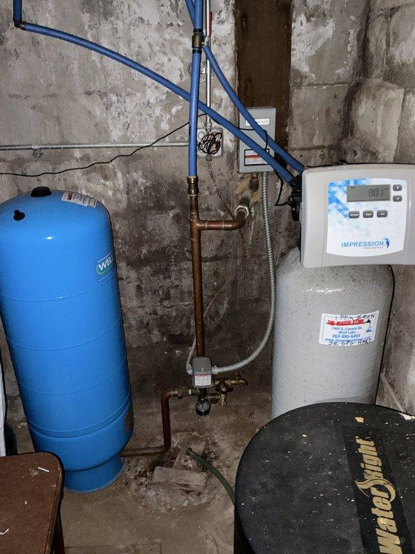 Completed comprehensive whole home plumbing inspection of residential property. Evaluated and documented all visible plumbing systems including water supply lines, drainage systems, fixtures, and mechanical equipment. 

Inspected basement utility area containing water pressure system with blue WE-branded pressure tank connected via blue PEX supply lines and copper piping with brass fittings and valves. Verified pressure gauge readings and assessed condition of tank connections and fittings. Examined wall-mounted Impression digital control panel and associated white cylindrical storage tank for proper operation and signs of wear.

Evaluated AO Smith water heater installation including top-mounted black pump assembly, electrical connections, and gas supply lines. Inspected copper and flexible metal tubing connections for leaks or corrosion. Assessed water heater drain pan installation and verified proper placement. Checked all visible piping including white PVC drainage lines and metalli