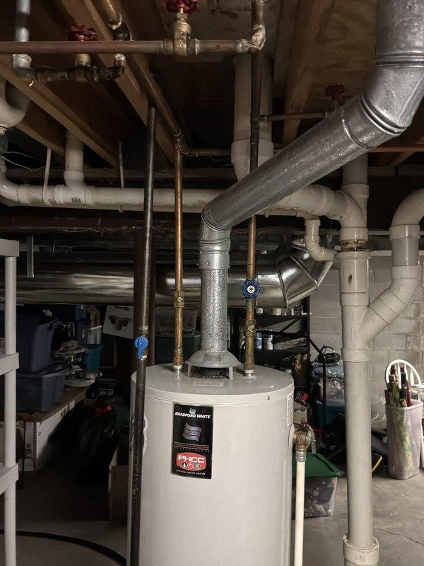 Conducted comprehensive water heater assessment in basement utility area and evaluated hot water distribution issue affecting kitchen sink. Inspected existing white cylindrical water heater unit, examined all supply and return piping connections, copper supply lines with shutoff valves, and verified proper venting configuration through galvanized ductwork. Documented current system condition including PVC drainage lines, pressure relief valve operation, and overall mechanical space layout to provide accurate replacement estimate and identify cause of inadequate hot water delivery to kitchen fixture.
