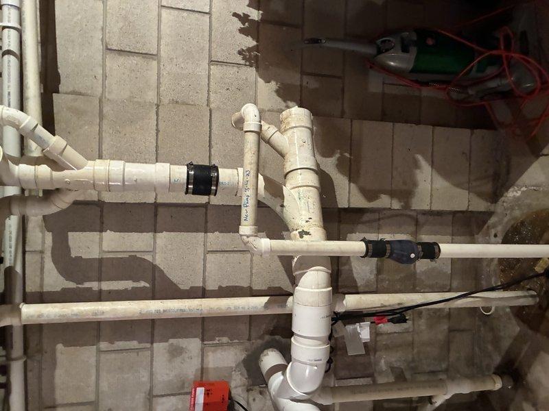 Successfully removed and replaced deteriorated cast iron piping that was penetrating through the concrete block wall. Installed new white PVC piping system with proper fittings, couplings, and black rubber connectors to ensure secure connections throughout the assembly. The replacement included multiple horizontal and vertical pipe runs with appropriate elbow joints and transitions to accommodate the existing plumbing configuration in the utility room.