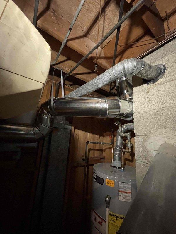 Completed HVAC ductwork installation in basement utility area. Installed metallic rigid ductwork with proper mounting brackets and ceiling supports, including elbow transitions for optimal airflow routing. Connected flexible and rigid ductwork to water heater exhaust system with appropriate venting materials and reflective insulation wrapping to meet code requirements for safe operation.