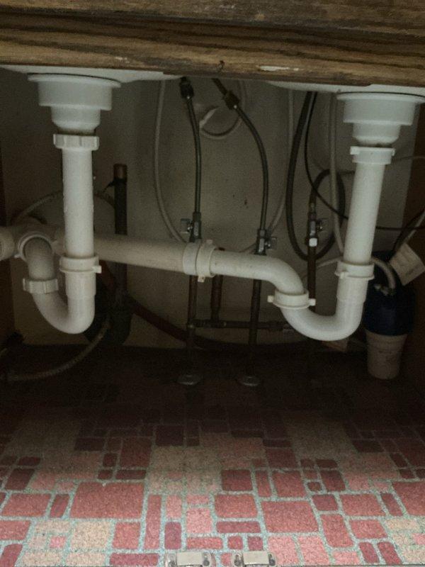 Replaced gooseneck single-handle kitchen faucet with chrome finish fixtures, including side sprayer attachment and soap dispenser. Installed new supply lines and P-trap assemblies for double-basin sink configuration. Customer also reported water softener and iron filter system cycling nightly between 9:59-11:00 PM, which appears to be operating on its programmed regeneration schedule.