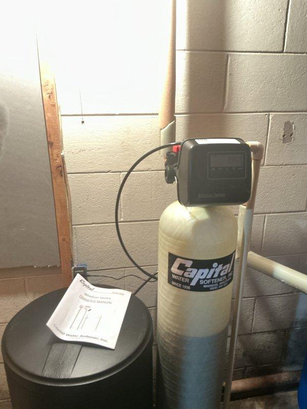 Completed installation of Spitfire brand water softener system in residential basement utility area. Unit was properly positioned, connected to existing copper water supply lines, and equipped with control head for automated operation. All plumbing connections were secured and tested for proper function. System was left operational with installation documentation provided on-site.