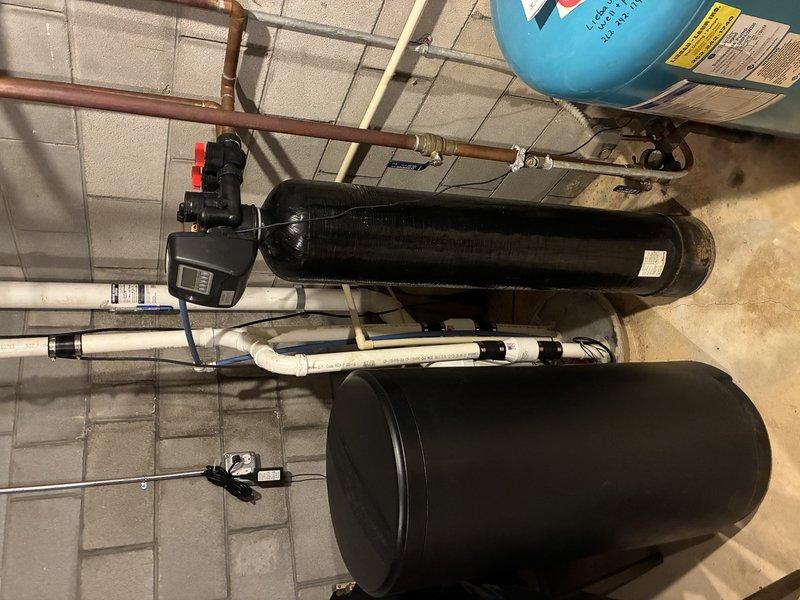 Responded to customer complaint of foul odor emanating from household water supply. Upon inspection of basement utility area, evaluated existing water treatment system including pressure tank, water softener unit, and associated plumbing connections. Assessed water quality issue and determined odor likely caused by bacterial growth in water heater or deteriorated anode rod. Documented existing equipment configuration with photographs showing pressure tanks, water softener control unit, and copper piping connections for service records and potential system upgrades.