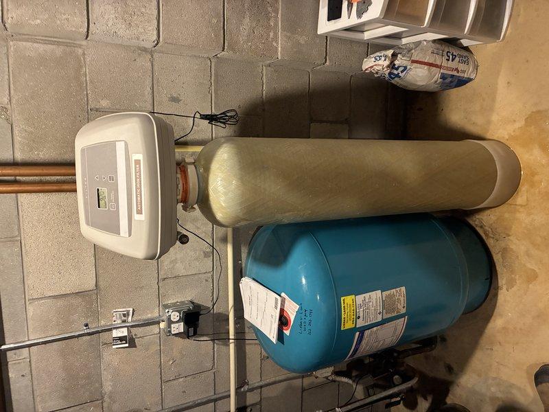 Responded to customer complaint of foul odor emanating from household water supply. Upon inspection of basement utility area, evaluated existing water treatment system including pressure tank, water softener unit, and associated plumbing connections. Assessed water quality issue and determined odor likely caused by bacterial growth in water heater or deteriorated anode rod. Documented existing equipment configuration with photographs showing pressure tanks, water softener control unit, and copper piping connections for service records and potential system upgrades.