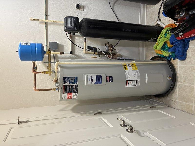 Completed installation of residential tanked water heater system in utility closet, including all necessary plumbing connections, expansion tank, pressure regulation components, and safety devices. Configured copper and PEX piping with brass fittings to integrate new water heater with existing household water supply lines, installed blue expansion tank with proper mounting and connections, and verified all components meet code requirements for safe operation.