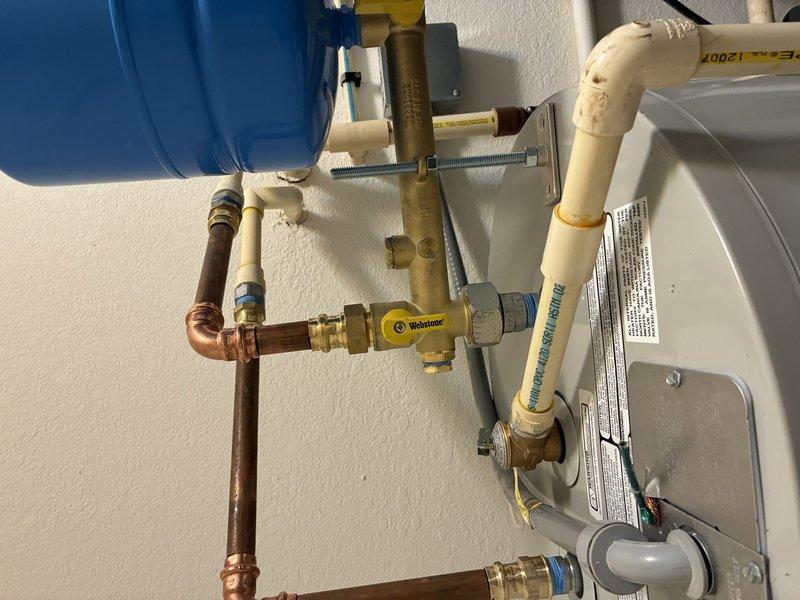 Completed installation of residential tanked water heater system in utility closet, including all necessary plumbing connections, expansion tank, pressure regulation components, and safety devices. Configured copper and PEX piping with brass fittings to integrate new water heater with existing household water supply lines, installed blue expansion tank with proper mounting and connections, and verified all components meet code requirements for safe operation.