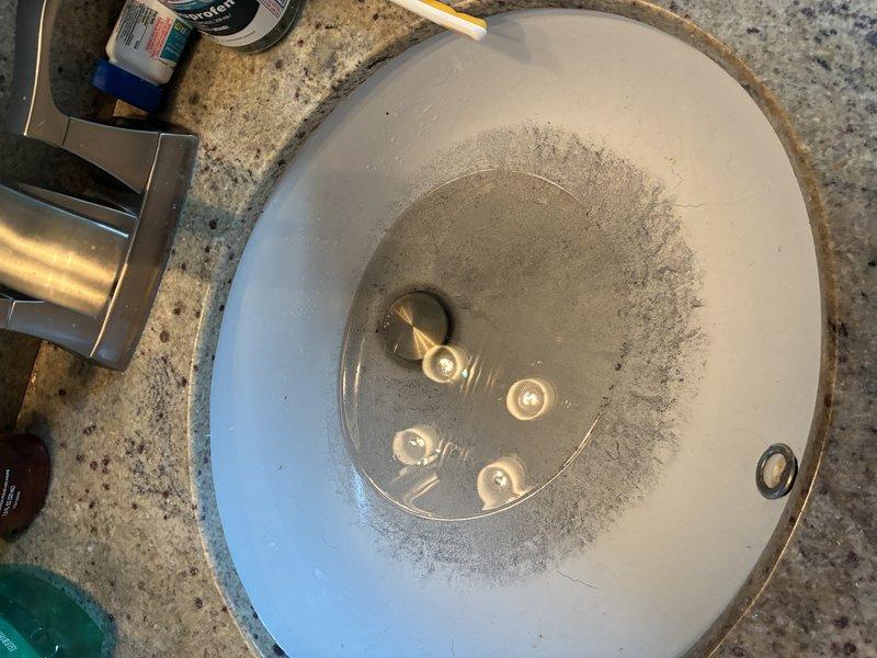 Responded to customer complaint of grayish-black sediment discharging from shower fixture during operation. Performed diagnostic inspection of plumbing system, including examination of water heater (approximately 11 years in service), supply lines, and bathtub/shower assembly. Documented sediment accumulation in both sink basin and bathtub, with concentrated deposits visible around drain areas. Inspected tub condition and noted significant deterioration of basin surface coating with exposed substrate material. Identified sediment consistent with water heater tank corrosion and mineral buildup typically associated with aging units nearing end of service life. Photographed affected fixtures showing gray particulate matter accumulation. Provided assessment findings and discussed replacement options for water heater to resolve sediment issue and prevent further system degradation.