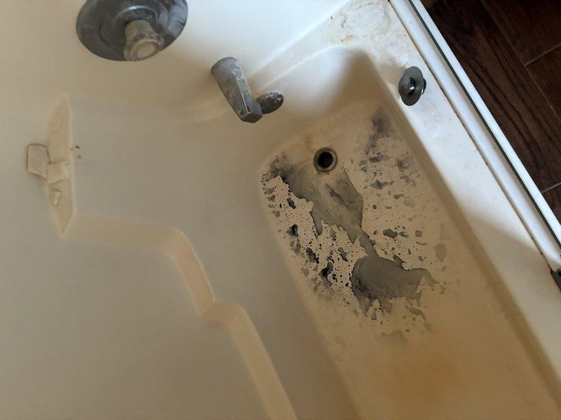 Responded to customer complaint of grayish-black sediment discharging from shower fixture during operation. Performed diagnostic inspection of plumbing system, including examination of water heater (approximately 11 years in service), supply lines, and bathtub/shower assembly. Documented sediment accumulation in both sink basin and bathtub, with concentrated deposits visible around drain areas. Inspected tub condition and noted significant deterioration of basin surface coating with exposed substrate material. Identified sediment consistent with water heater tank corrosion and mineral buildup typically associated with aging units nearing end of service life. Photographed affected fixtures showing gray particulate matter accumulation. Provided assessment findings and discussed replacement options for water heater to resolve sediment issue and prevent further system degradation.