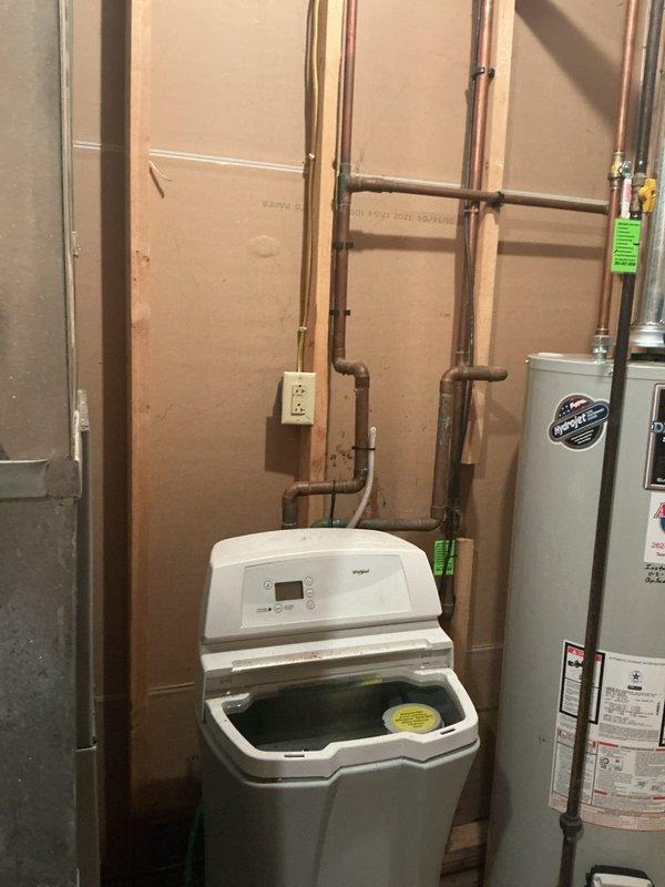 Performed diagnostic service on Whirlpool water softener experiencing complete drainage failure. Inspected unit installation, control panel functionality, and associated plumbing connections including copper supply and drain lines. Documented equipment condition and utility room configuration with water heater proximity for service records.