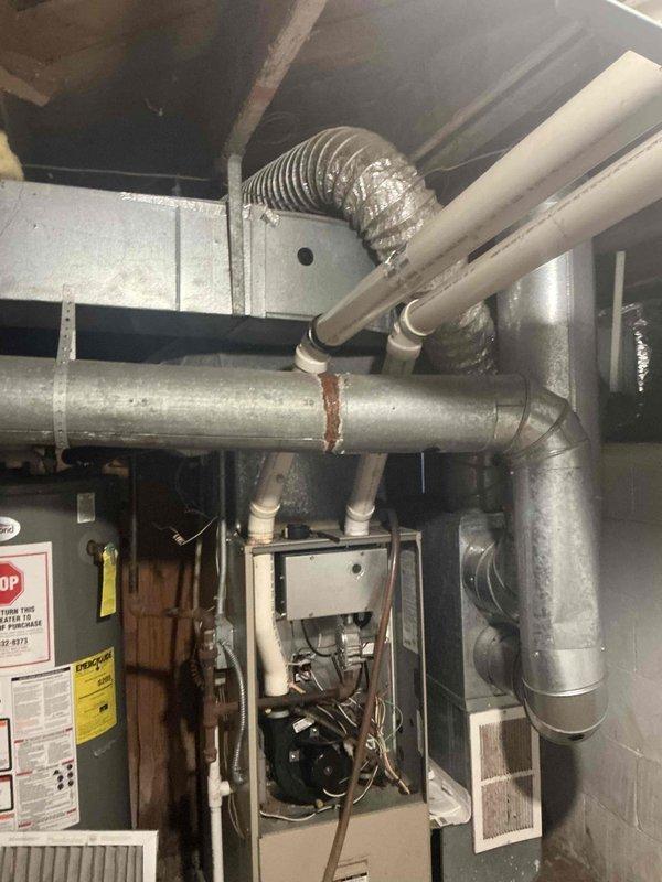 Responded to emergency furnace service request and conducted comprehensive system assessment for replacement estimate. Evaluated existing HVAC equipment in mechanical room, including furnace unit with blower motor assembly, associated ductwork system with flexible and rigid metal components, and refrigerant line configuration. Documented current installation conditions including white metal housing unit with ventilation grilles, copper refrigerant tubing, and green metal base panel for replacement specifications and proposal preparation.